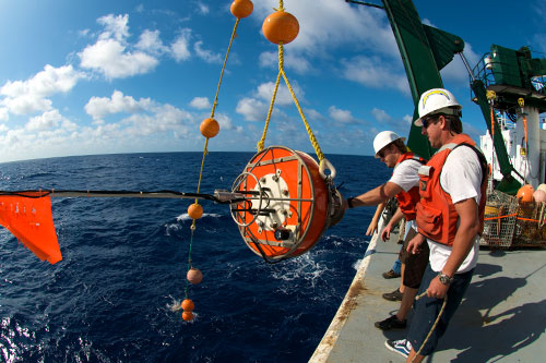 Researcher out on the ocean on a large vessel hauling up a buoy to collect data.